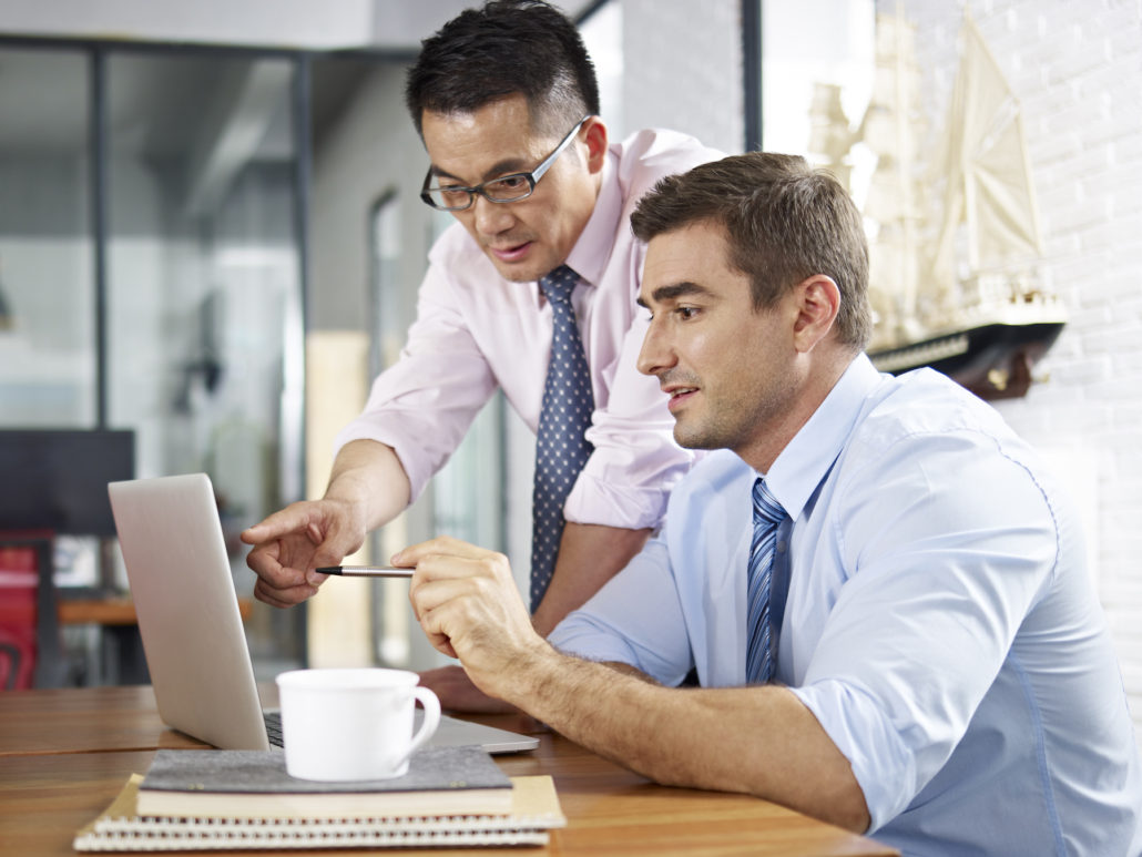 asian and caucasian business executives looking at laptop screen while having a discussion in a multinational company.